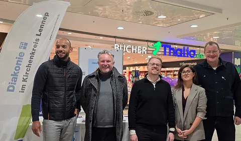 Fünf Menschen stehen in einem Einkaufscentrum vor dem Eingang zu Thalia. Links neben den lächelnden Menschen sieht man ein Werbebanner mit der Aufschrift Diakonie im Kirchenkreis Lennep.