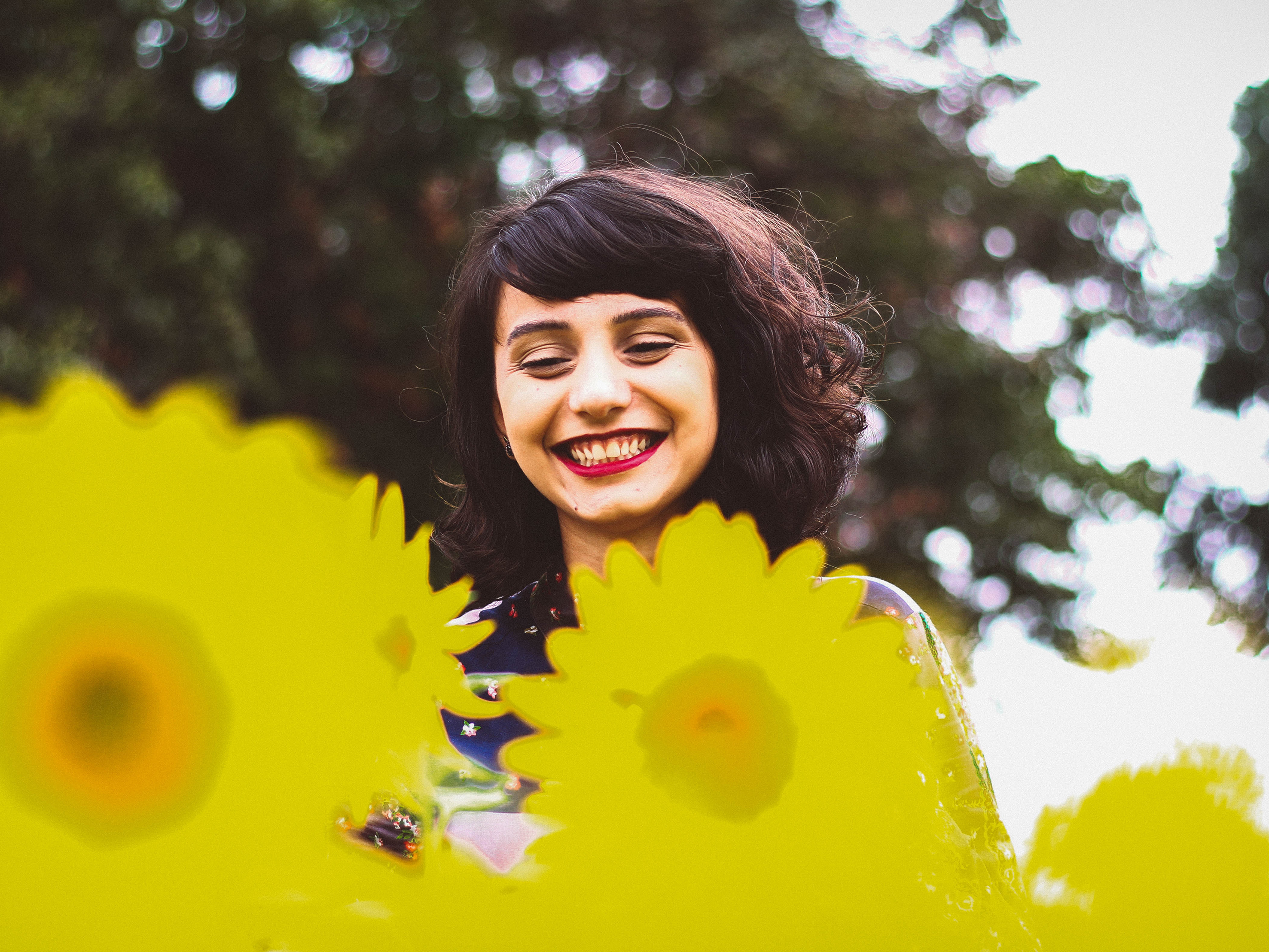 Lächelnde Frau mit roten Lippen, umgeben von gelben Blumen.