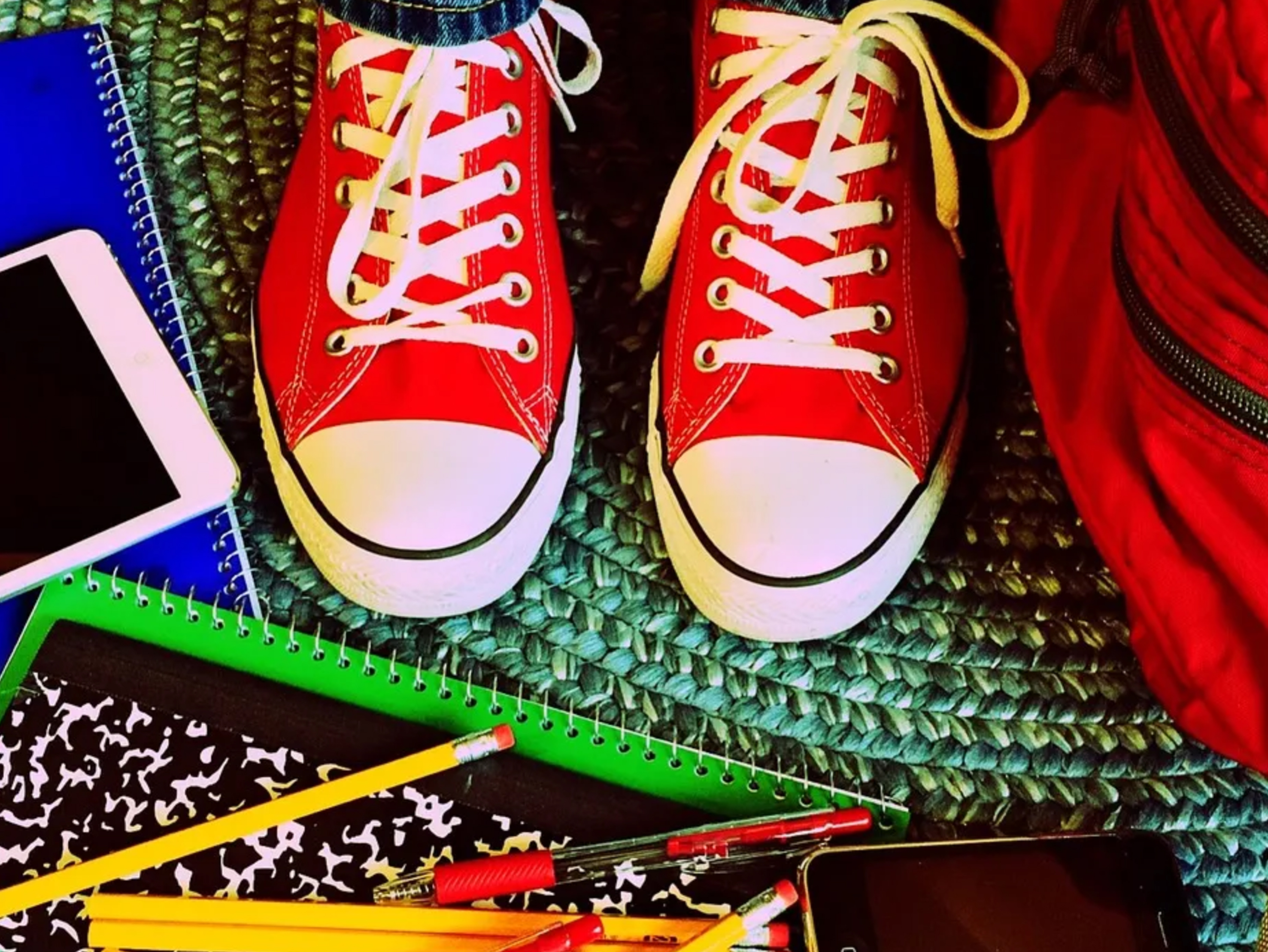 Rote Turnschuhe und Schulmaterial auf einem bunten Teppich.