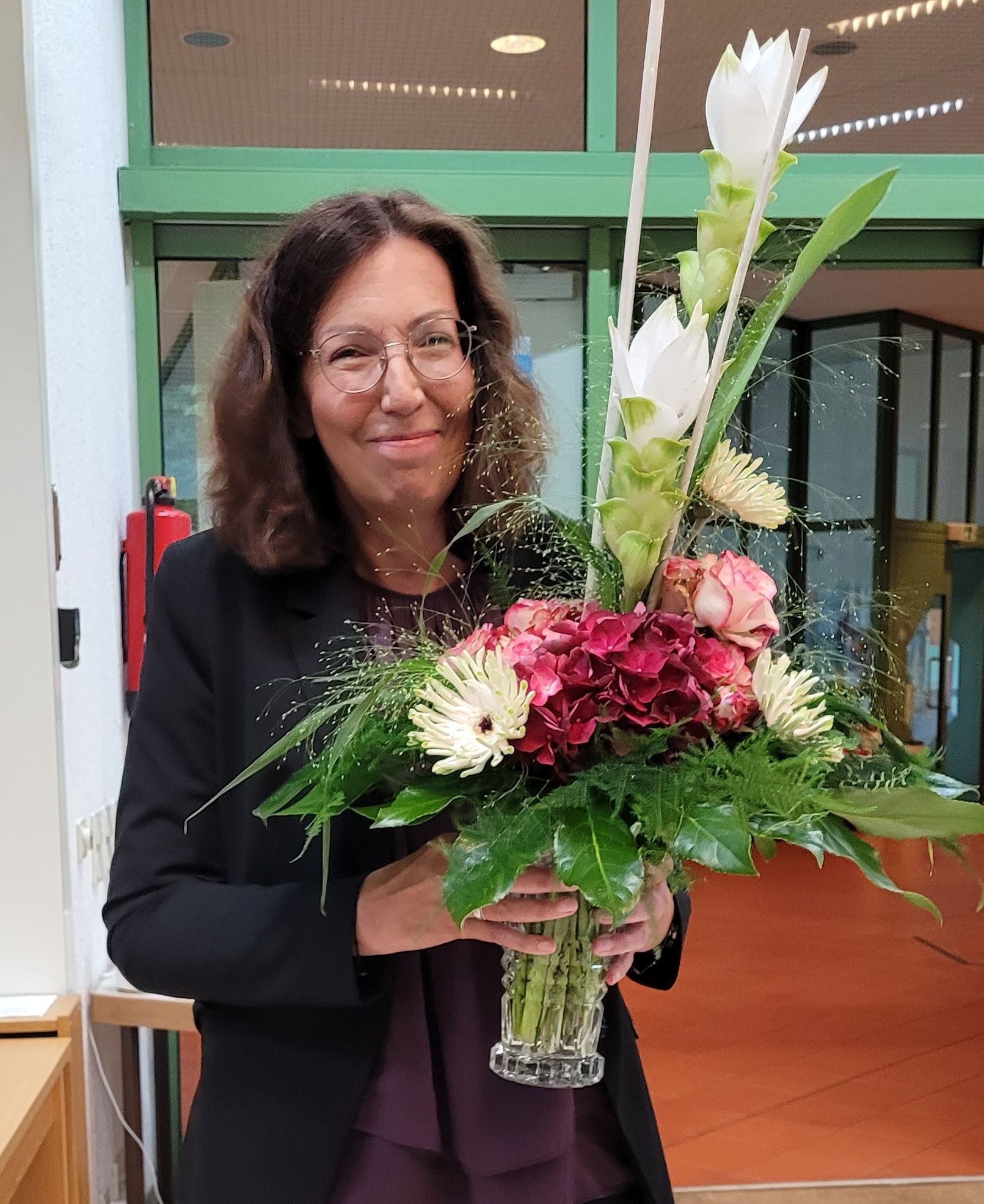 Eine lächelnde Frau in einem Türrahmen mit einem großen Blumenstrauß und breit lächelnd