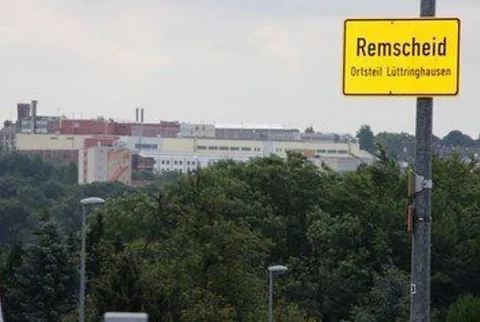 Gelbes Ortsschild Remscheid vor Gebäuden und Bäumen.